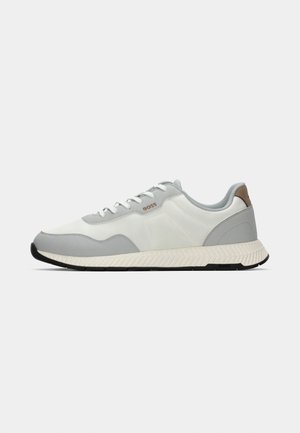 Sneakers with a white and light grey textile upper, featuring a brown accent at the heel and a textured white sole with black tread.