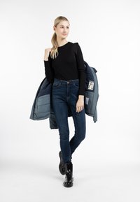 Top nero a maniche lunghe con dettagli sulle spalle, jeans skinny blu scuro e giacca blu gonfiata, accompagnati da stivaletti neri alla caviglia.