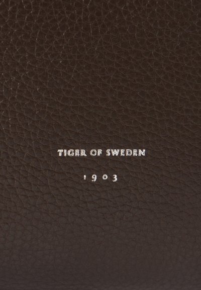 Pruun tekstureeritud nahk, millel on reljeefne logo "TIGER OF SWEDEN" ja "1903" hõbedases värvuses, rõhutades meisterlikkust ja kvaliteeti.