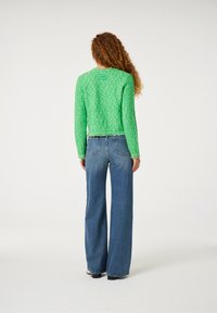Groene textuurtrui met lange mouwen, cropped ontwerp en onafgewerkte zoom, gecombineerd met hooggewaaid lichte blauwe jeans.