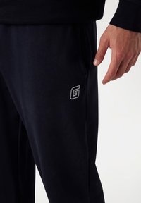 Námornícke jogger nohavice vyrobené z mäkkého materiálu, s bočnou kapsou a malým šedým logom "G" na stehne. Slim fit dizajn s elastickým pásom.