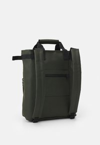 Grön tygryggsäck med en strukturerad form, dubbla handtag och vadderade remmar. Har ett framfick med blixtlås och strukturerad yta.