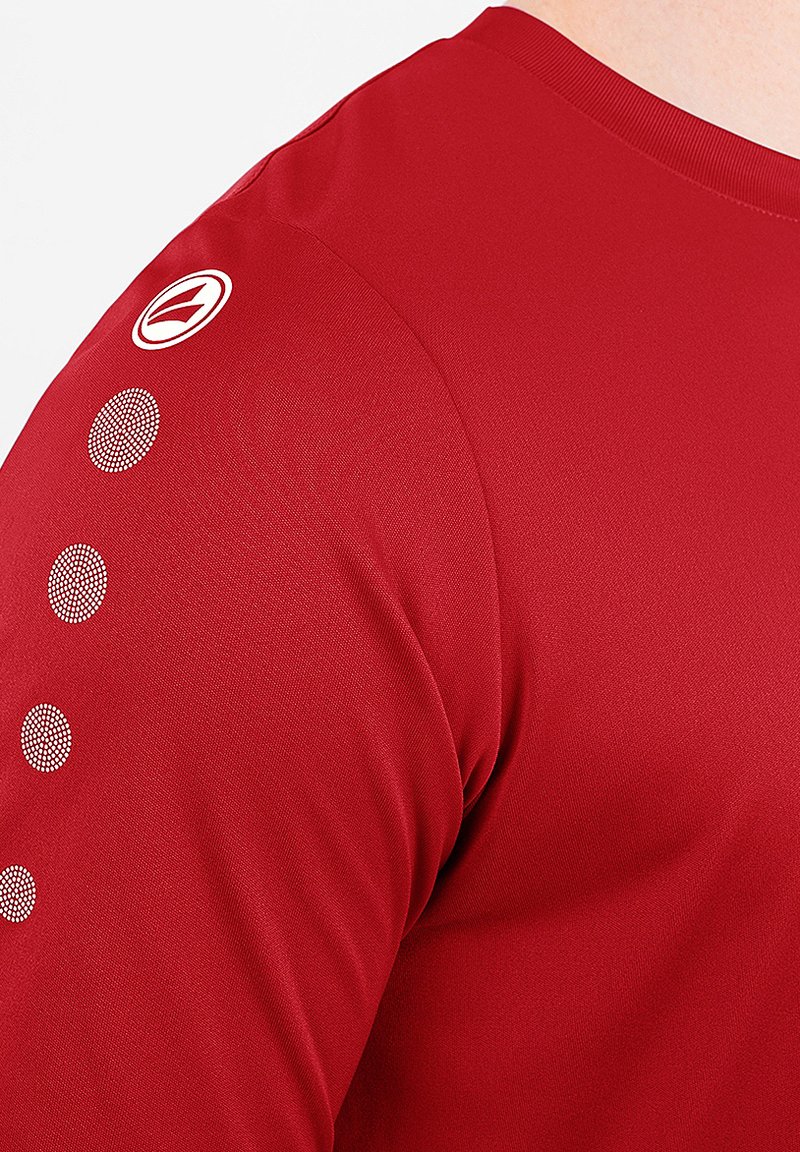 Red long-sleeve shirt made of smooth fabric. Features a logo and three dotted accents on the shoulder, with a crew neckline.