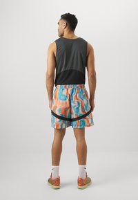 Top sin mangas negro y gris, pantalones cortos de patrón colorido con acentos en azul, naranja y negro, combinados con zapatillas deportivas multicolores y calcetines blancos.