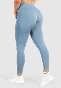 Hoge taille legging in lichtblauwe stof met een gladde textuur, met een aangesloten silhouet en accent naden. Gecombineerd met witte sneakers.