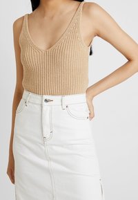 Harmaa neulottu toppi syvällä V-päällä ja leveillä olkaimilla, yhdistetty valkoinen farkkuhame sivuaukkoilla ja kontrastivärillä ompeleet.