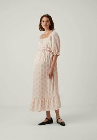 Svetlo roza maksi obleka z cvetličnim vzorcem, kvadratnim izrezom, napihnjenimi rokavi in zbranim pasom. Ima nabran rob in tekoč material.