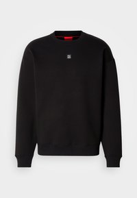 Sweat-shirt noir à manches longues col rond, avec poignets et ourlet côtelés, portant un petit logo carré "HUGO" centré sous l'encolure.