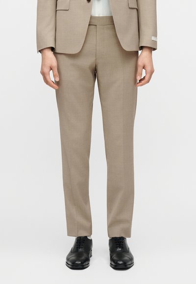 Μπεζ ραμμένο παντελόνι από υφασμάτινη υφή, με στενή γραμμή, ίσια πόδια, σε συνδυασμό με μαύρα δερμάτινα παπούτσια.