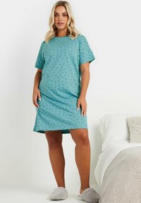 Una camicia da notte turchese con maniche corte e stampa a stelle. Realizzata in tessuto morbido, arriva sopra il ginocchio, abbinata a pantofole grigie e morbide.
