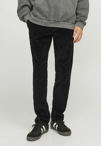 Black corduroy pants with a straight fit, featuring vertical ribbed texture. Worn with a gray hoodie and black sneakers with white accents.