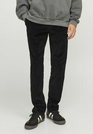 Black corduroy pants with a straight fit, featuring vertical ribbed texture. Worn with a gray hoodie and black sneakers with white accents.