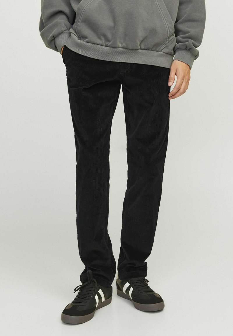Black corduroy pants with a straight fit, featuring vertical ribbed texture. Worn with a gray hoodie and black sneakers with white accents.