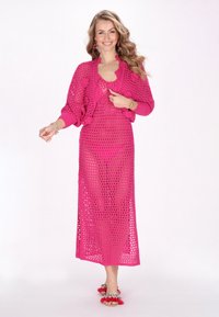 Cardigan in maglia rosa aperta e abito coordinato, con un motivo geometrico, maniche lunghe e spacchi laterali. Tessuto leggero e testurizzato.