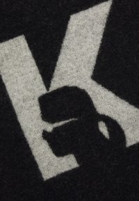 Sort og grå tekstil med et fremtrædende hvidt bogstav "K" og en silhuetdesign, med en blød, tekstureret overflade.