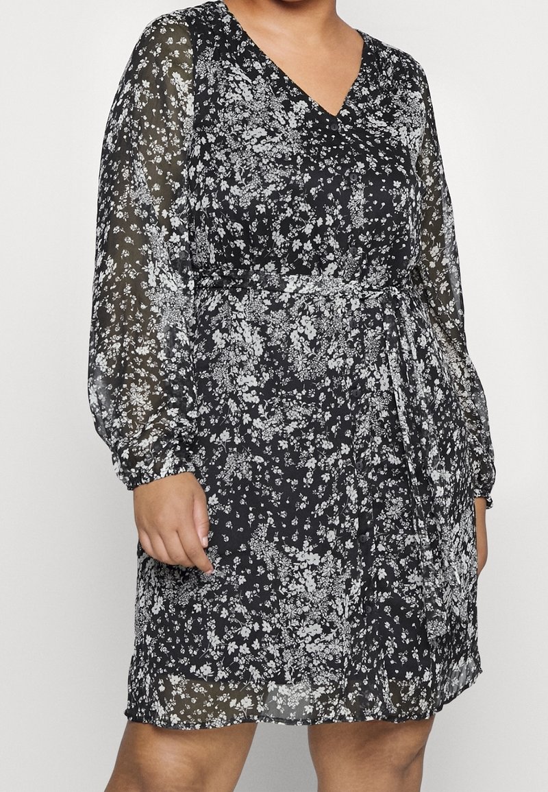 Vestido negro con flores, mangas largas transparentes, escote en forma de v, cintura ceñida y una falda fluida con un patrón de flores blancas.