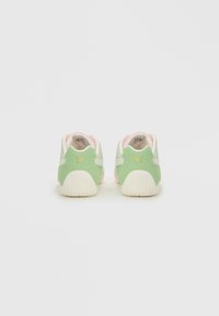 Een paar lichtgroene en witte Puma-sneakers met een gouden logo op de hakken, gezien van achteren op een witte achtergrond.