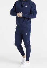 Navy blue hoodie and joggers made of soft fabric; features a front pocket, drawstring hood, and logo on the chest and thigh.