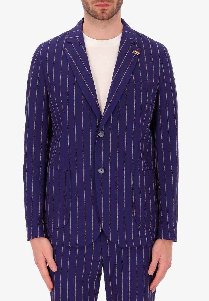 Blazer blu navy con righe verticali dorate, due tasche frontali, revers a punta e chiusura a due bottoni. Il tessuto appare strutturato.