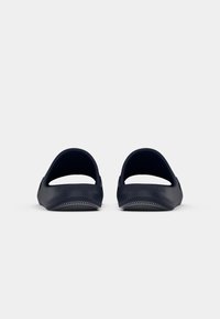 Marine slip-on sandaler laget av fleksibelt materiale med en glatt finish, åpen bak og teksturert såle. Merkevare synlig på siden.