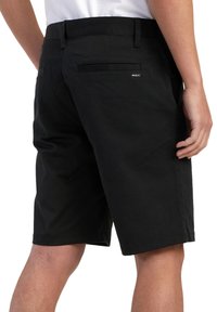 Pantalones cortos negros hechos de tejido ligero, con un bolsillo trasero, una etiqueta de logo y un corte recto con un dobladillo limpio.