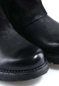 Bottes noires en cuir et en suède avec bouts arrondis et semelles épaisses en caoutchouc cousues sur fond blanc.