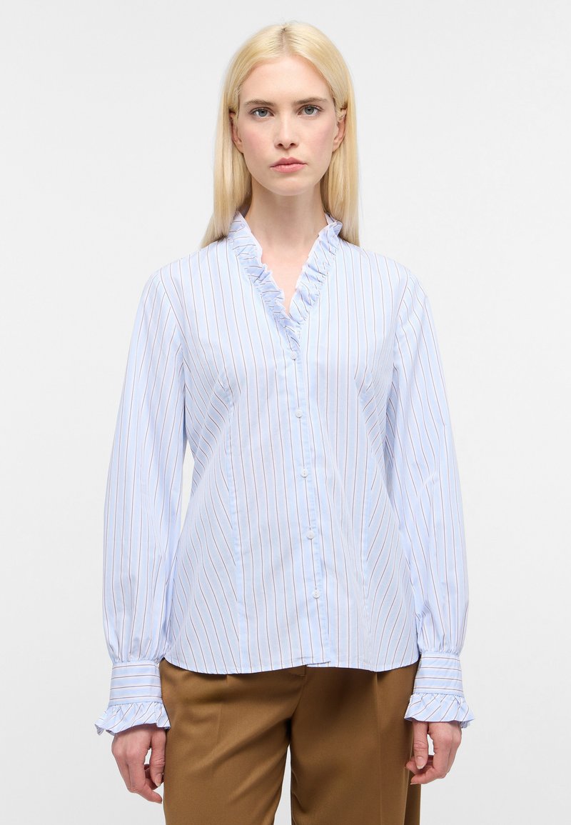 Blusa a righe azzurro chiaro con scollo a sbuffo, chiusura con bottoni e maniche lunghe a palloncino. Il tessuto sembra morbido e leggero.