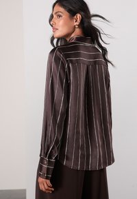 Braunes Satinhemd mit Knopfleiste, weißen vertikalen Streifen, klassischem Kragen, langen Ärmeln mit geknöpften Manschetten und einem Rückenpasse-Detail.