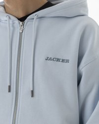 Šviesiai mėlynas zip-up megztinis, pagamintas iš minkštos medžiagos, su kengūros kišene, kontrastinga siuvinėta užrašu "JACKER" ir sidabro spalvos aksesuarais.