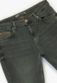 Pantalones vaqueros de mezclilla verde oscuro con corte ajustado, que cuentan con cierre de botón, cinco bolsillos y detalles de costura en contraste. Talla W32 L32.