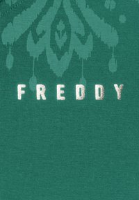 Tela verde azulado con un patrón texturizado y letras metálicas plateadas que forman la palabra "FREDDY". El material parece ser suave y acanalado.