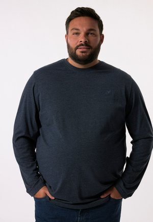 Langärmliges navy-blaues Hemd aus weichem Stoff, mit Rundhalsausschnitt und dezentem Logo auf der Brust. Kombiniert mit Jeans.