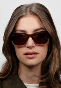 Occhiali da sole con montatura rettangolare di colore marrone scuro e lenti a gradiente, caratterizzati da bordi lisci e un design minimalista.