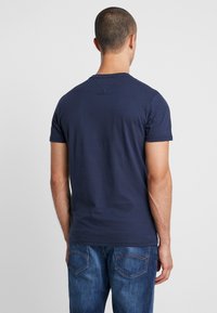 Navy blue short-sleeve t-shirt with a crew neck, made from cotton, featuring a smooth texture and minimal design. Back view shows a v-stitch detail.