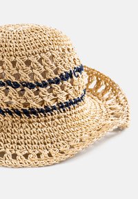 Spleciony kapelusz ze słomy o otwartym wzorze. Naturalny kolor brązowy z niebieskimi plecionkami i szerokim rondem dla ochrony przed słońcem.