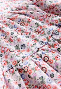 Weicher Stoff mit einem detaillierten Blumenmuster, das rote, violette, blaue und grüne Blumen auf hellem Hintergrund zeigt, mit gesammelter Naht.