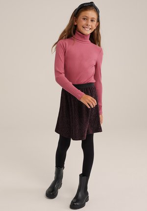 Pink gerippter Rollkragenpullover, schwarzer Strukturrock, schwarze Strumpfhosen und schwarze Absatzstiefeletten. Der Rock hat eine ausgestellte Form und einen subtilen Schimmer.