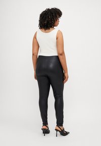 Fekete műbőr leggings fehér ujjatlan felsővel párosítva. Az öltözet illeszkedő kialakítással és sima textúrával rendelkezik.