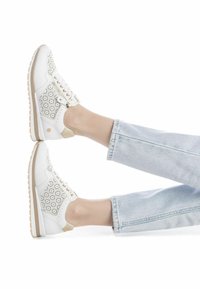 Zapatilla blanca con recortes florales en los laterales, acentos dorados y detalles en beige. Suela media texturizada y cordones planos con cierre de cremallera.