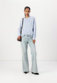 Light blue sweater, relaxed fit, long sleeves. Faded wide-leg jeans with a high waist. Model holds a small dark bag, wearing black shoes.