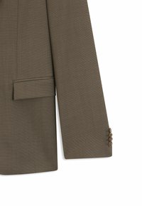 Olivgrön blazer gjord av strukturerad tyg. Har en plan ficka och tre knappar på ärmen. Strukturerad design med skräddarsydd passform.