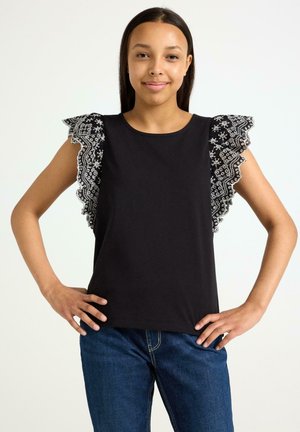 Haut noir avec des manches en dentelle volantes à motif floral, col rond et coupe décontractée, associé à un jean bleu.