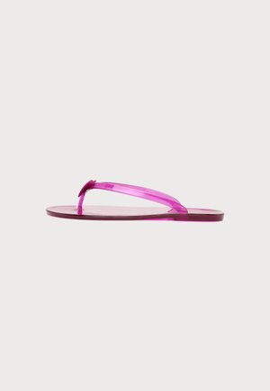Ένα μονό διάφανο ροζ σανδάλι flip-flop με λεπτά λουράκια και επίπεδη σόλα σε απλό φωτεινό φόντο.