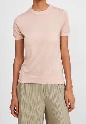 Maglietta a maniche corte in maglia di un rosa chiaro con scollatura rotonda, texture liscia e orlo a coste, abbinata a pantaloni chiari con pieghe.