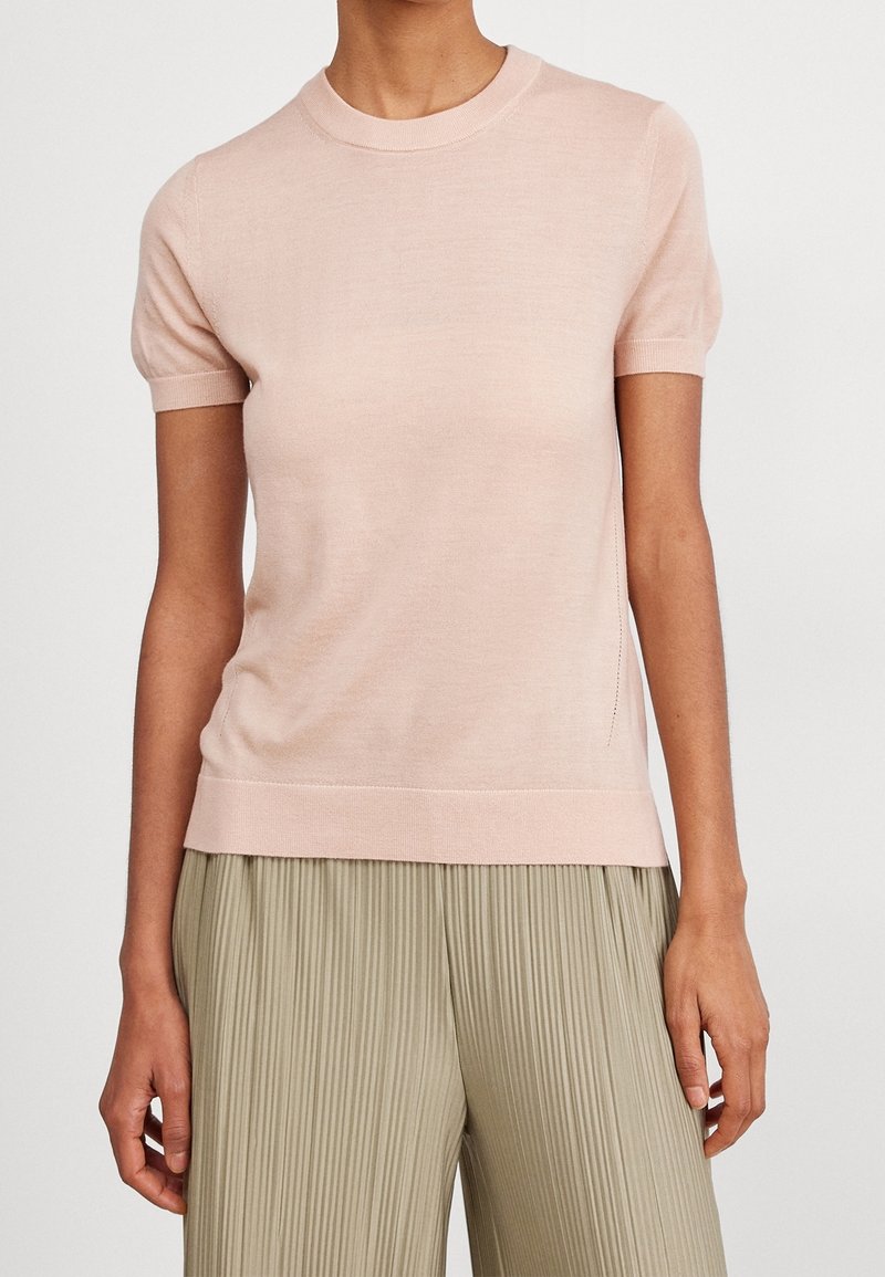 Světlé růžové pletené tričko s krátkým rukávem a kulatým výstřihem, hladkým povrchem a žebrovaným lemem, spárované s skládacími světlými kalhotami.