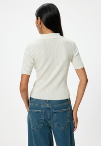 Witte geribbelde polo t-shirt met korte mouwen, aansluitend design en een klassieke kraag, gecombineerd met hoog-waisted blauwe denim jeans.