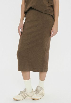 Jupe marron à mi-longueur en tissu doux avec une texture lisse, associée à des baskets beiges et des chaussettes blanches à la cheville.