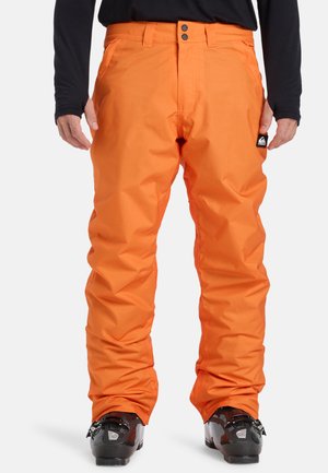 Pantalons de neige orange vif avec une coupe ample, fabriqués en matériau imperméable. Présente des boutons à l'avant doublés et un logo de marque sur la poche gauche.