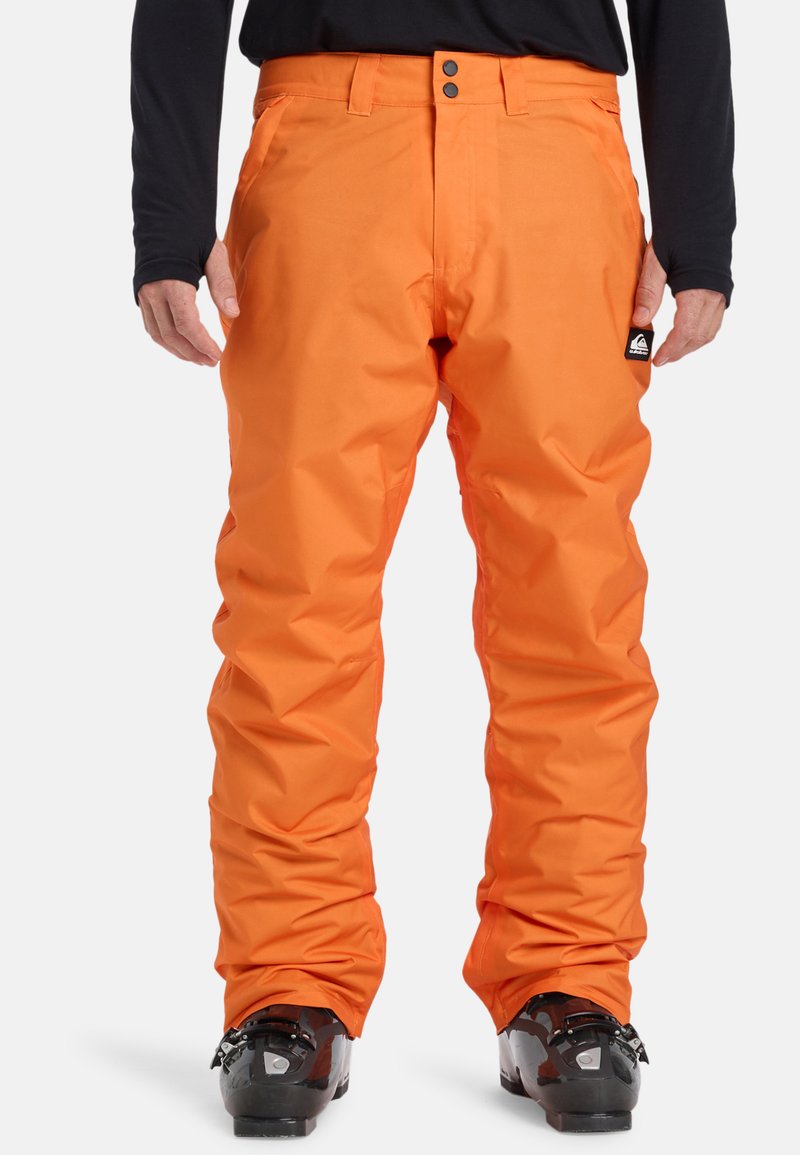 Jasnooranžové snežné nohavice s voľným strihom, vyrobené z vodoodpudivého materiálu. Obsahujú dvojité predné gombíky a firemné logo na ľavom vrecku.