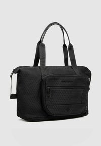 Bolsa de lona negra con un patrón de triángulos texturizados, asas dobles y un bolsillo frontal con cremallera. Fabricada con tela resistente y detalle sutil de la marca.